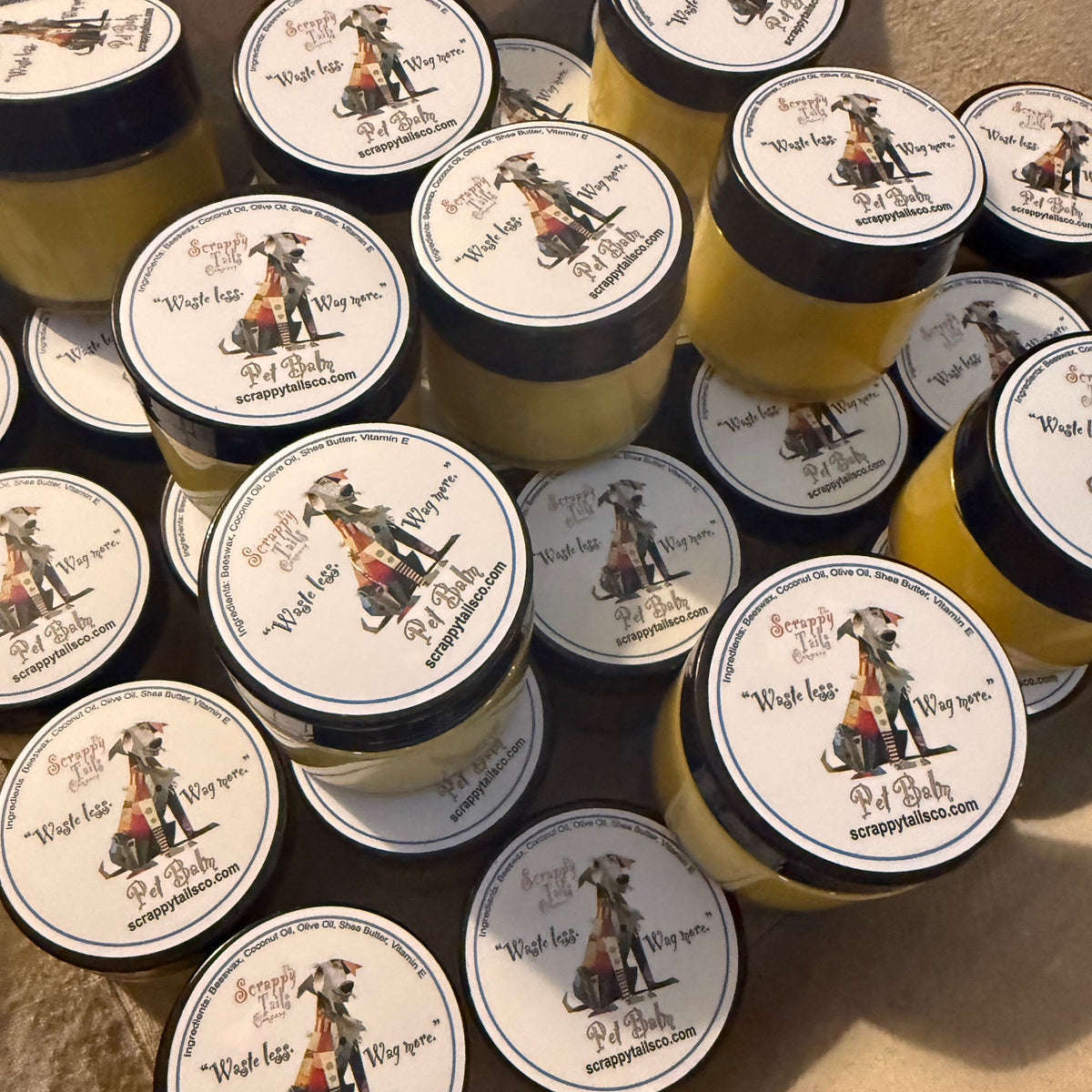 Multiple small jars of yellow cream or balm with black lids and round white labels featuring a pirate illustration and the text 'Wish lip, Wish eye, Wish arm, Wish leg, Wish foot, Wish hair, Wish skin, Wish you,' arranged on a beige fabric background.