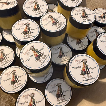 Multiple small jars of yellow cream or balm with black lids and round white labels featuring a pirate illustration and the text 'Wish lip, Wish eye, Wish arm, Wish leg, Wish foot, Wish hair, Wish skin, Wish you,' arranged on a beige fabric background.