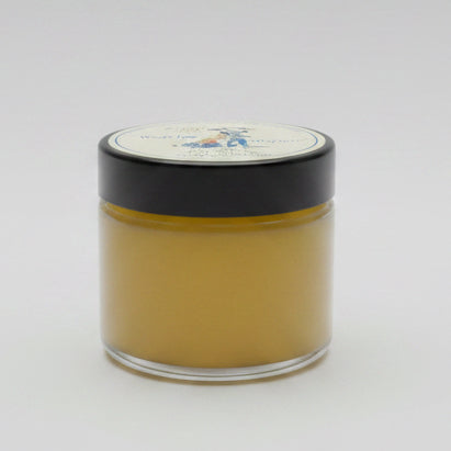A small clear jar filled with golden yellow wax or balm, topped with a black lid and a round white label, photographed on a plain light background.
